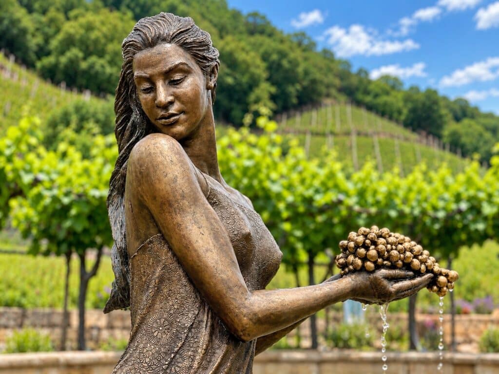 Bronzestatue einer Frau mit Trauben vor einem Weinberg